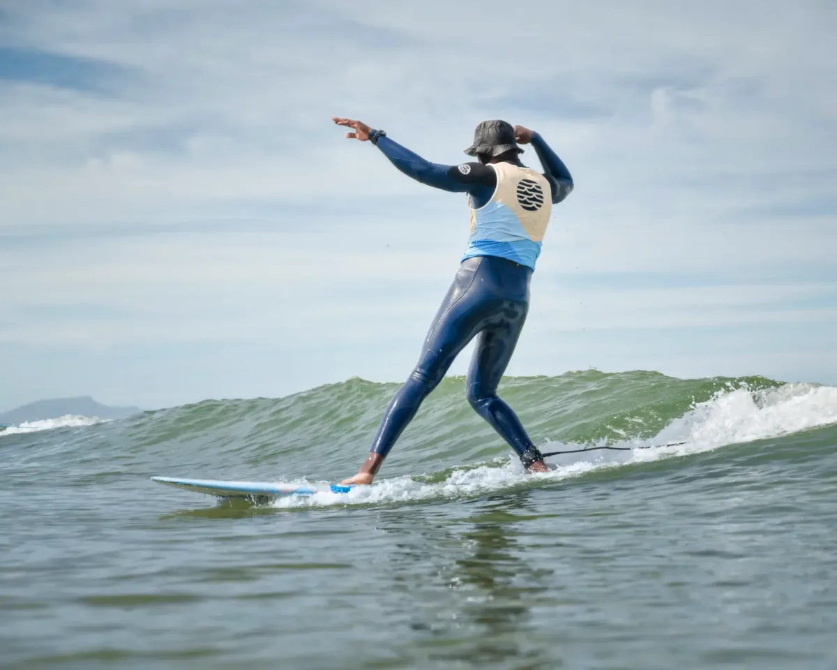 A surfer in a wetsuit with a blue and beige jersey, standing on a surfboard, riding a wave, as if he was dancing on water