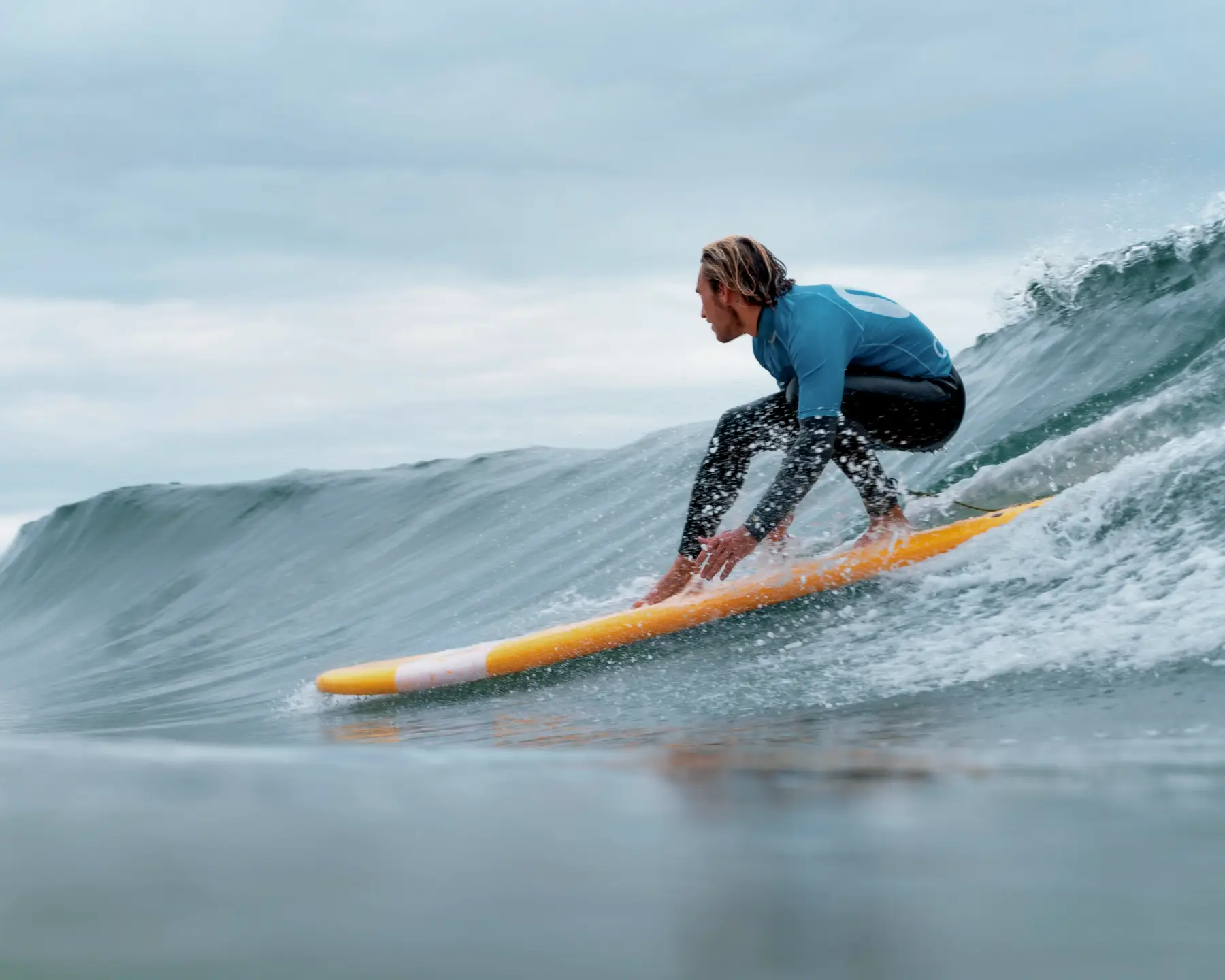 A focused surfer in a black and blue wetsuit performing a maneuver on a wave