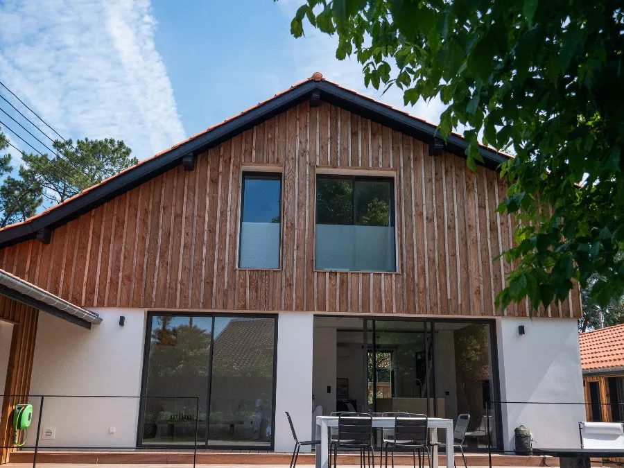 Rear façade of a contemporary house with timber cladding, white render, and a furnished terrace.