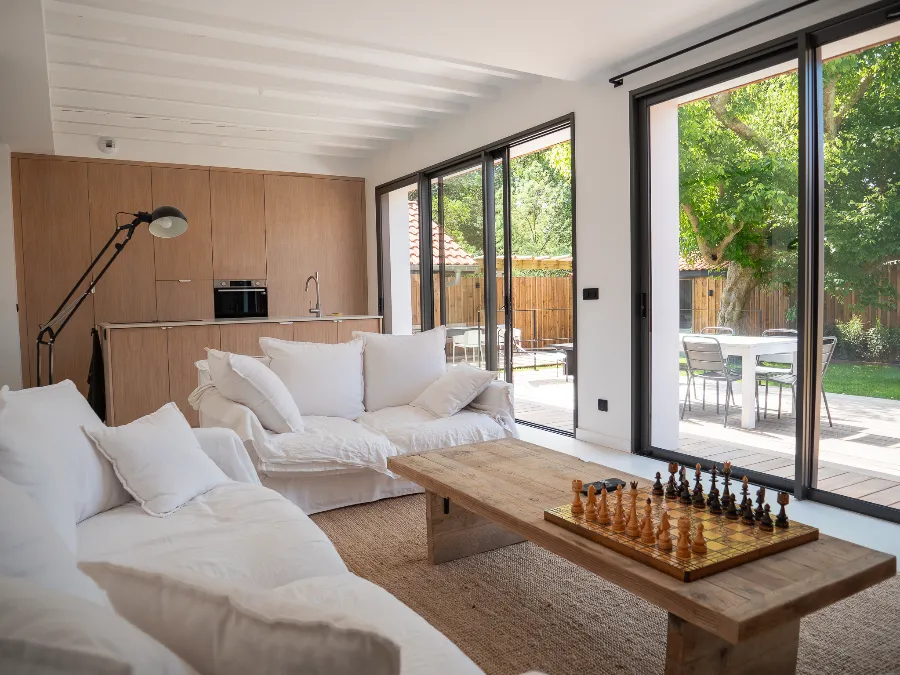 Bright living room with white sofas, a wooden coffee table, and an open-plan kitchen overlooking the garden.