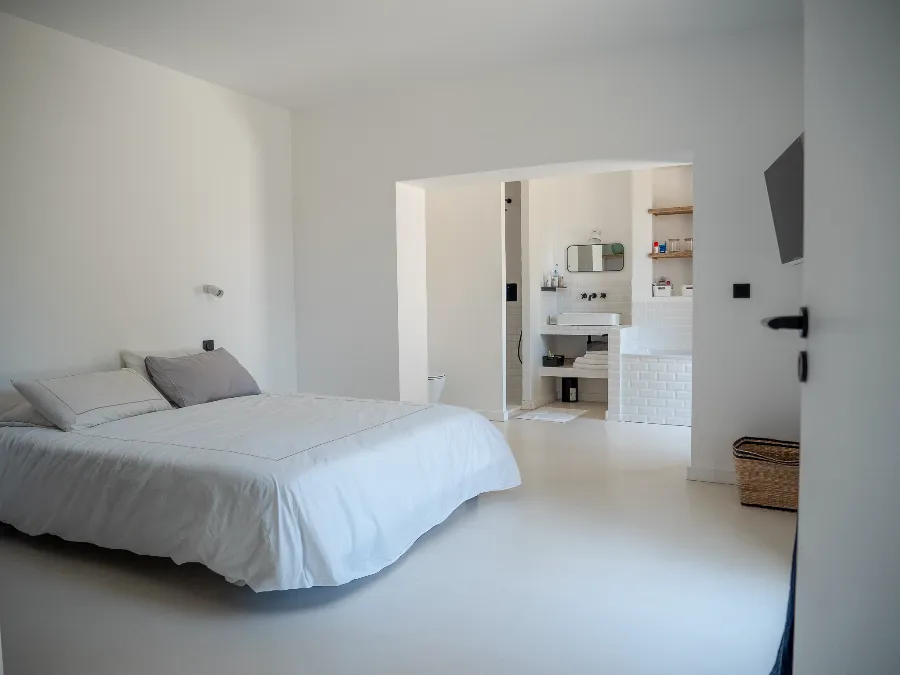 Minimalist white bedroom with a double bed and an open-plan bathroom.