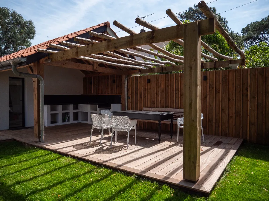 Wooden pergola covering a terrace with a dining table, chairs, and a lounge area.