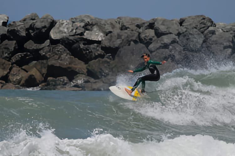 Un adolescent surfe devant un mur de rochers à Capbreton.